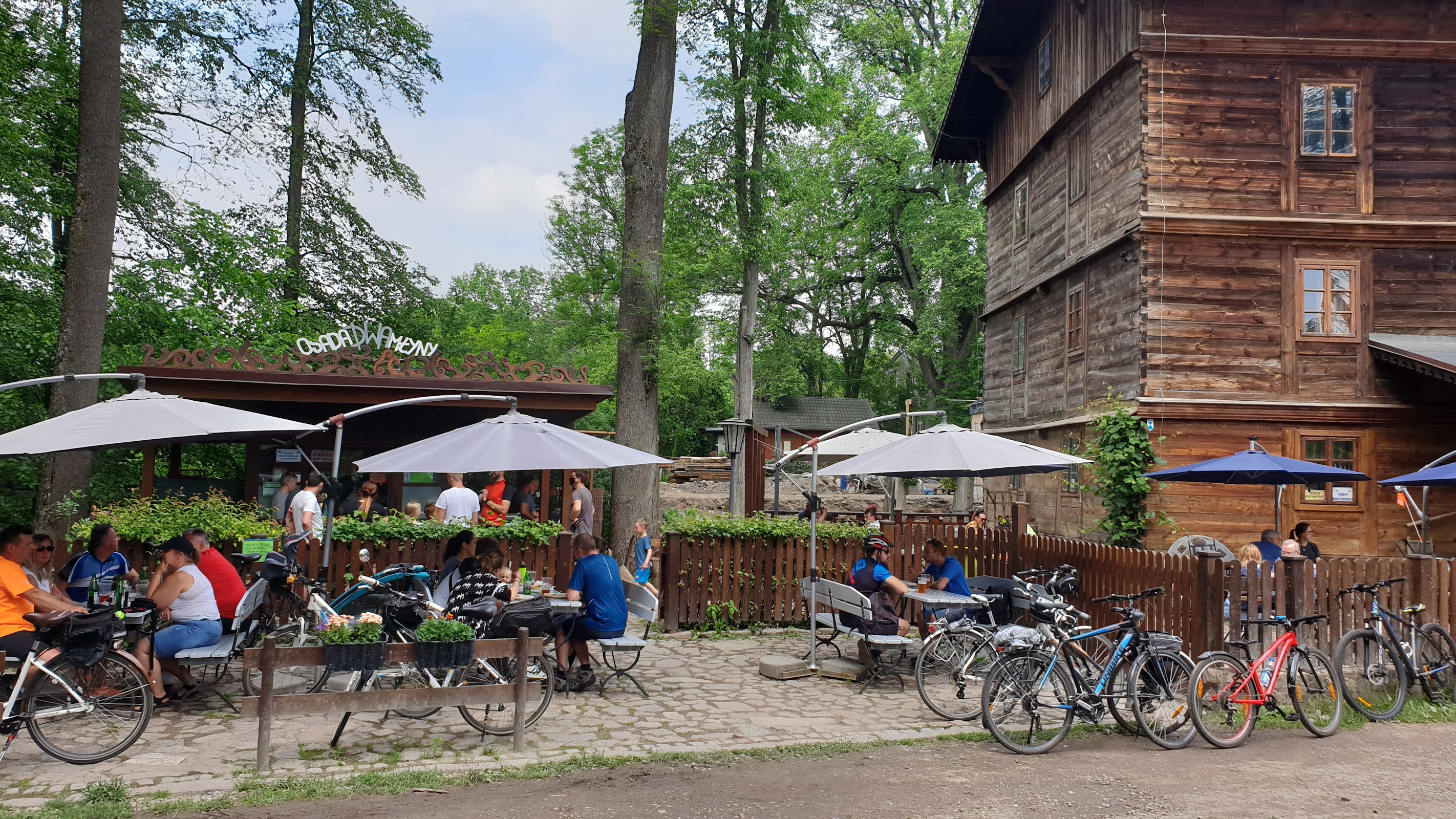 Bar i ogródek restauracyjny w Osadzie Dwa Młyny - stoliki pod parasolami, rowery przy płocie, drewniany młyn w tle
