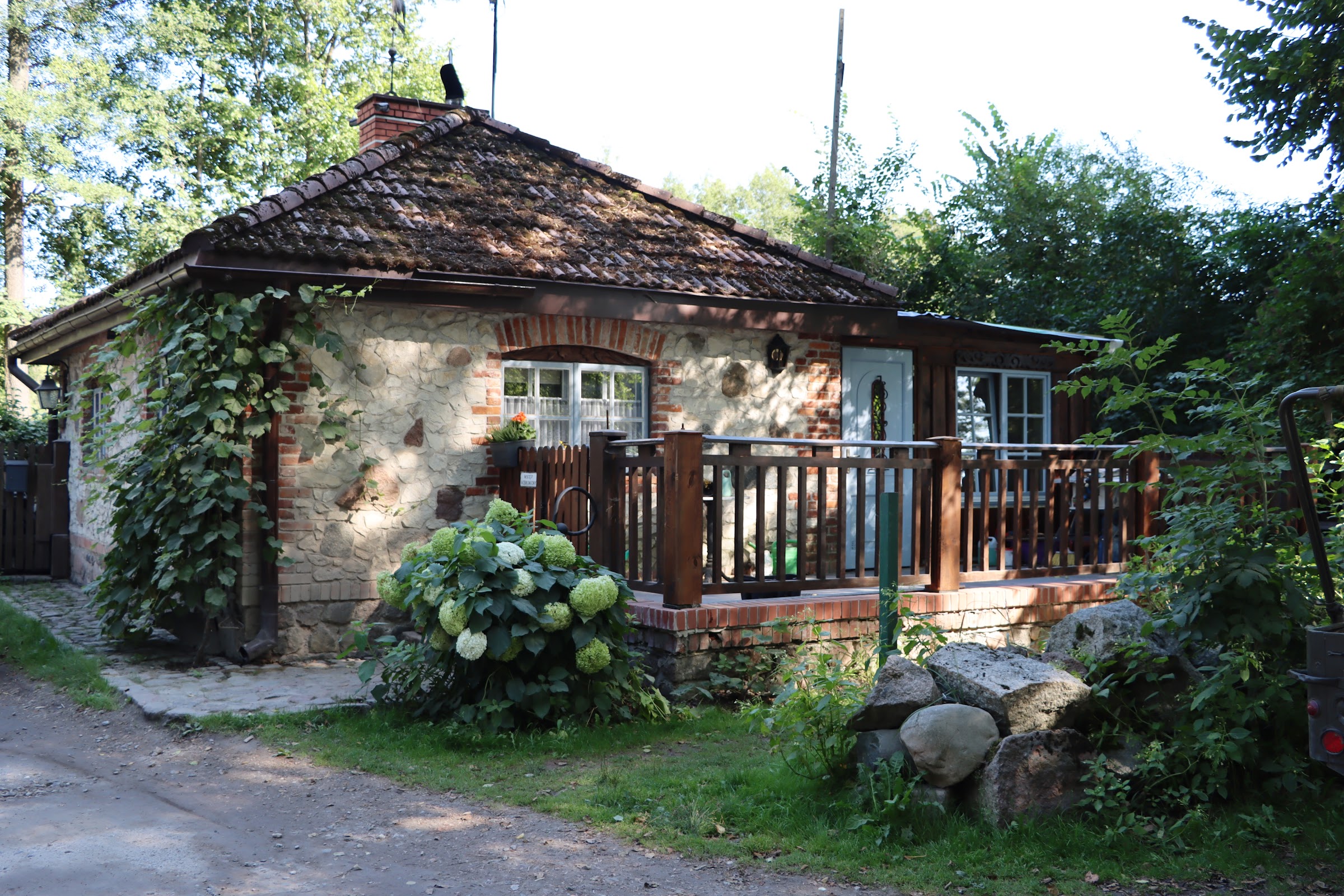 Stary kamienno-ceglany domek w Osadzie Dwa Młyny porośnięty bluszczem i hortensjami